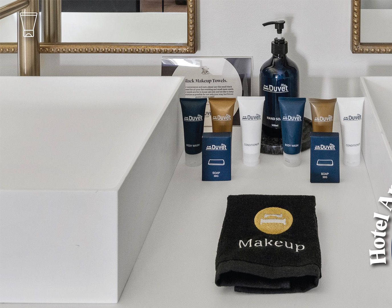 A bathroom vanity with a mirror, a black makeup towel, and various DuVét toiletries including body wash, conditioner, and soap.