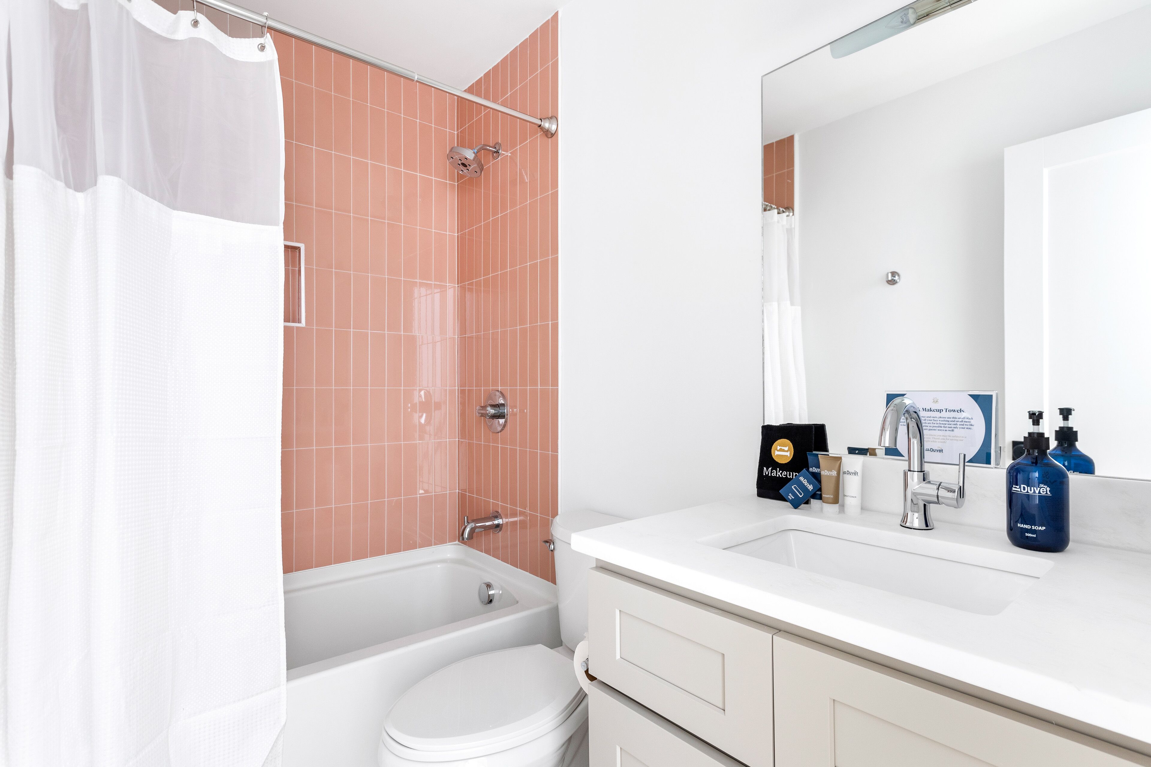 A bathroom with a white bathtub, a toilet, a sink with toiletries, and a shower with a curtain.