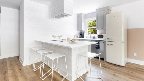 Una cocina moderna con armarios blancos, una isla central con taburetes y un microondas integrado, además de un refrigerador blanco.
