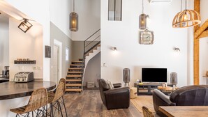 A modern kitchen with a bar area, a staircase, a living room with a sofa and TV, and a dining area. - Villa La Roche Rouge (Pougnadoresse)