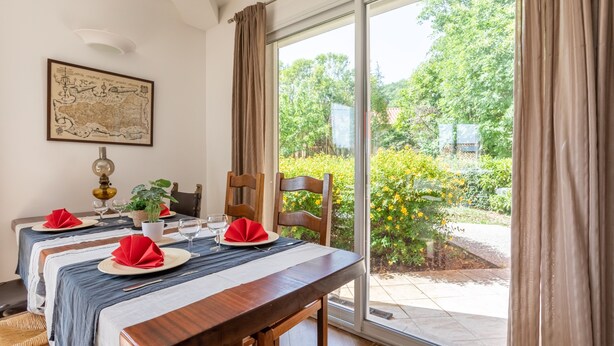 Un comedor con una mesa preparada para cuatro, un mapa en la pared y vistas a zonas verdes al exterior.