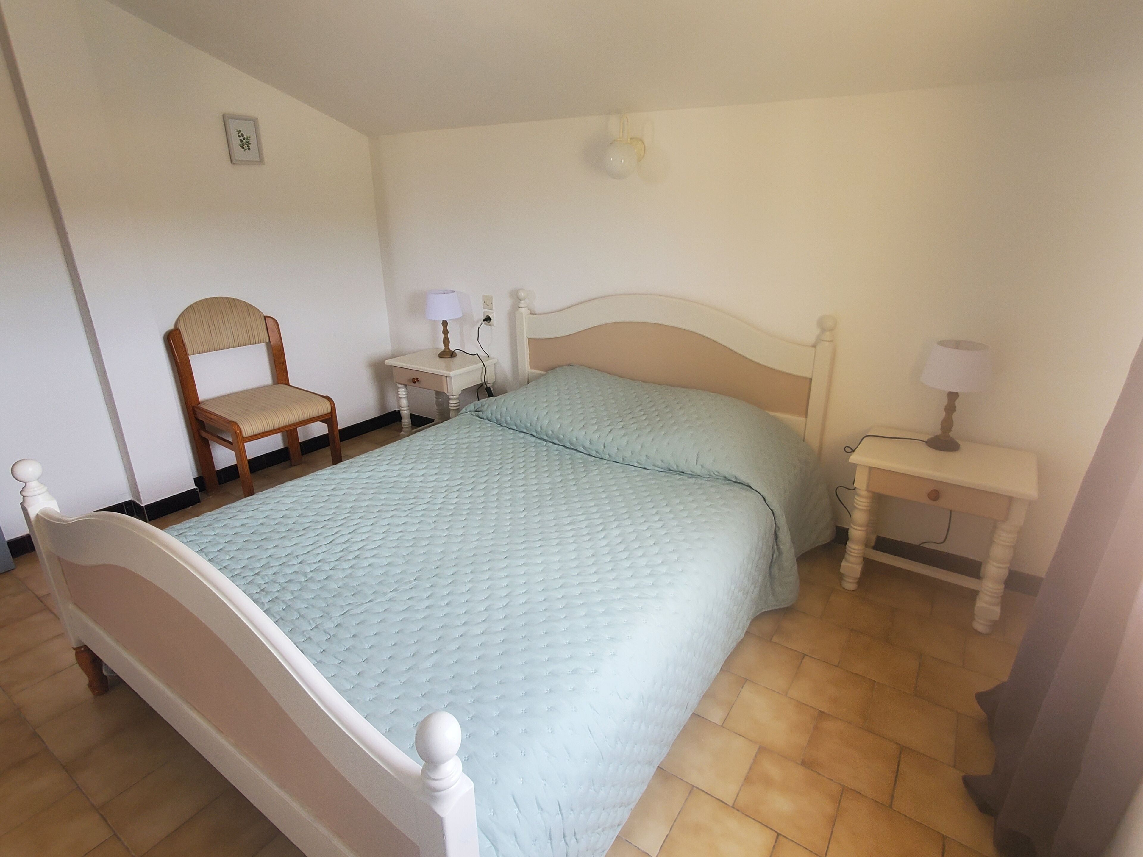 Ein Schlafzimmer mit einem Bett, einem Sessel, zwei Nachttischen mit Lampen und einer Wandleuchte.