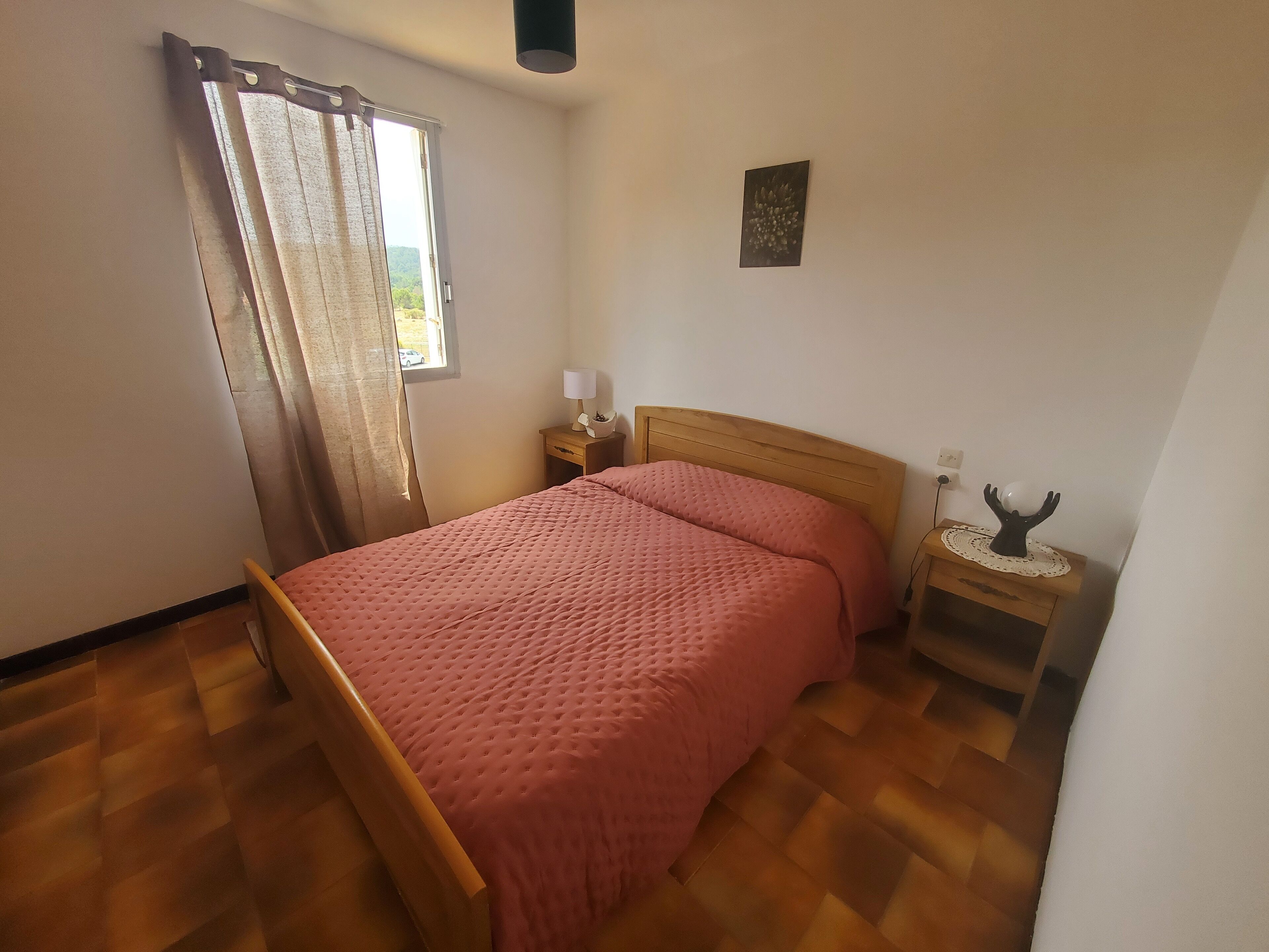 Un dormitorio con una cama de madera, una mesita de noche con lámpara y una ventana con cortinas.