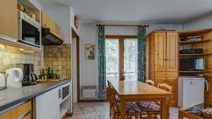 A compact kitchen with a dining area, wooden cabinets, a built-in oven, and a small refrigerator. - Le Col des Aravis - Two Bedroom Apartment, Sleeps 5 (La Giettaz)
