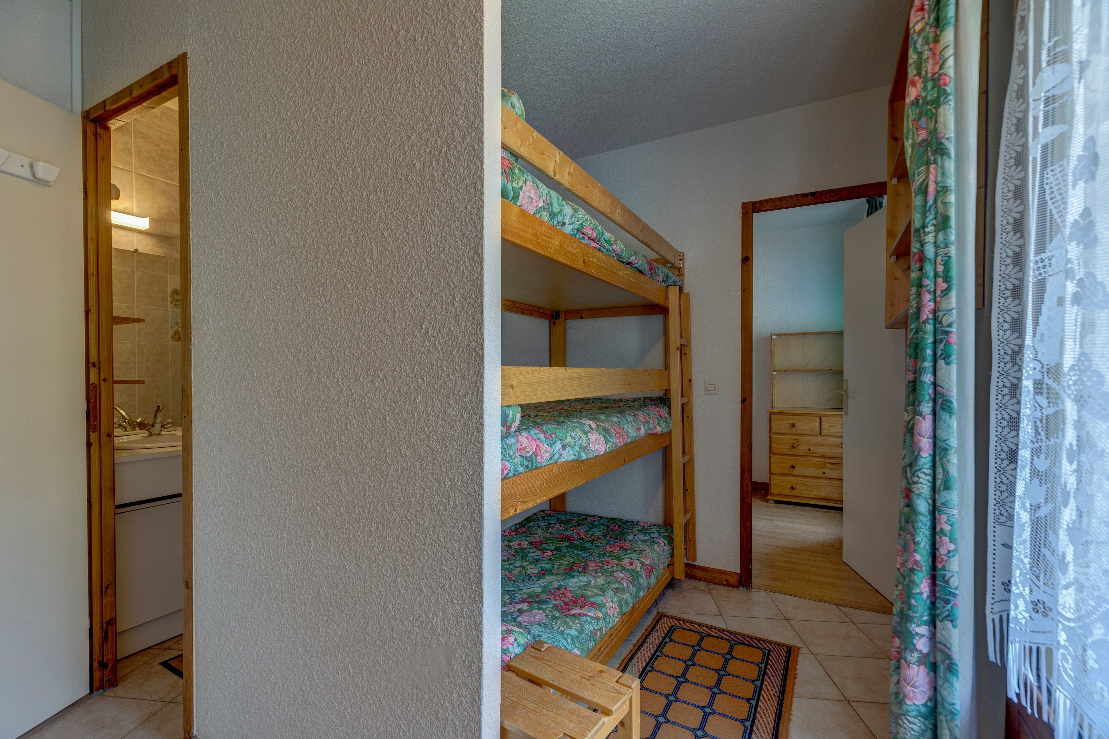Ein Zimmer mit Etagenbetten, einer Holzkommode und einem Badezimmer mit Waschbecken und Toilette.