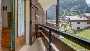 A wooden balcony with a view of a village and mountains. - Le Col des Aravis - Two Bedroom Apartment, Sleeps 5 (La Giettaz)