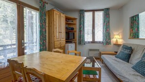 A cozy room with a wooden dining table, a sofa, and a cabinet with a television. - Le Col des Aravis - Two Bedroom Apartment, Sleeps 5 (La Giettaz)