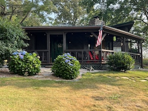 A wooden cabin with a covered porch, a stone chimney, and an American flag.