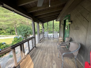 A wooden deck with outdoor seating, a green door, and a view of the surrounding greenery.