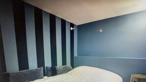 A bedroom with a large bed, striped wall panels, and a small wooden stool.