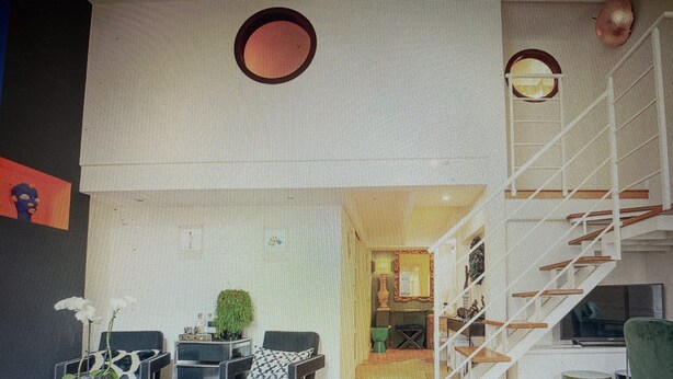 A modern living room with a staircase, a dining area, and a kitchen visible in the background.