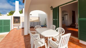 Terassi, jossa on valkoinen pöytä ja tuolit, grilli ja näkymä takapihalle.