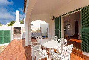 Eine Terrasse mit weißem Tisch und Stühlen, einem Grill und Blick auf den Garten.