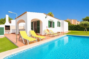 Un espace aménagé au bord de la piscine, avec un bâtiment blanc, des volets verts et des chaises longues jaunes.