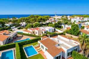 A coastal residential area with villas, a swimming pool, and a lighthouse in the background.