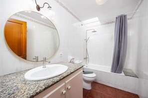 Ein Badezimmer mit rundem Spiegel, Waschbecken, Toilette und Dusche.
