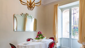 A dining area with a round table, red chairs, a white tablecloth, a chandelier, a mirror, and a window with curtains. - Capo 10 Liberty C3 - Two Bedroom Apartment, Sleeps 4 (Syracuse)