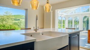 A modern kitchen with a large island, pendant lights, and a view of the outdoors. - Orchard Cottage (Ambleside)