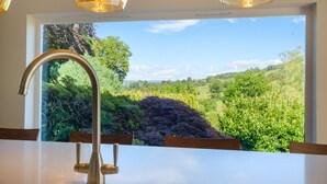 A bathroom with a large window, a modern faucet, and a view of a lush green landscape. - Orchard Cottage (Ambleside)