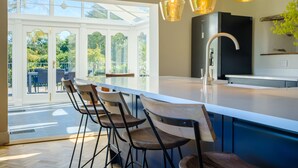A modern kitchen with a large island, bar stools, pendant lighting, and a view of the outdoors. - Orchard Cottage (Ambleside)