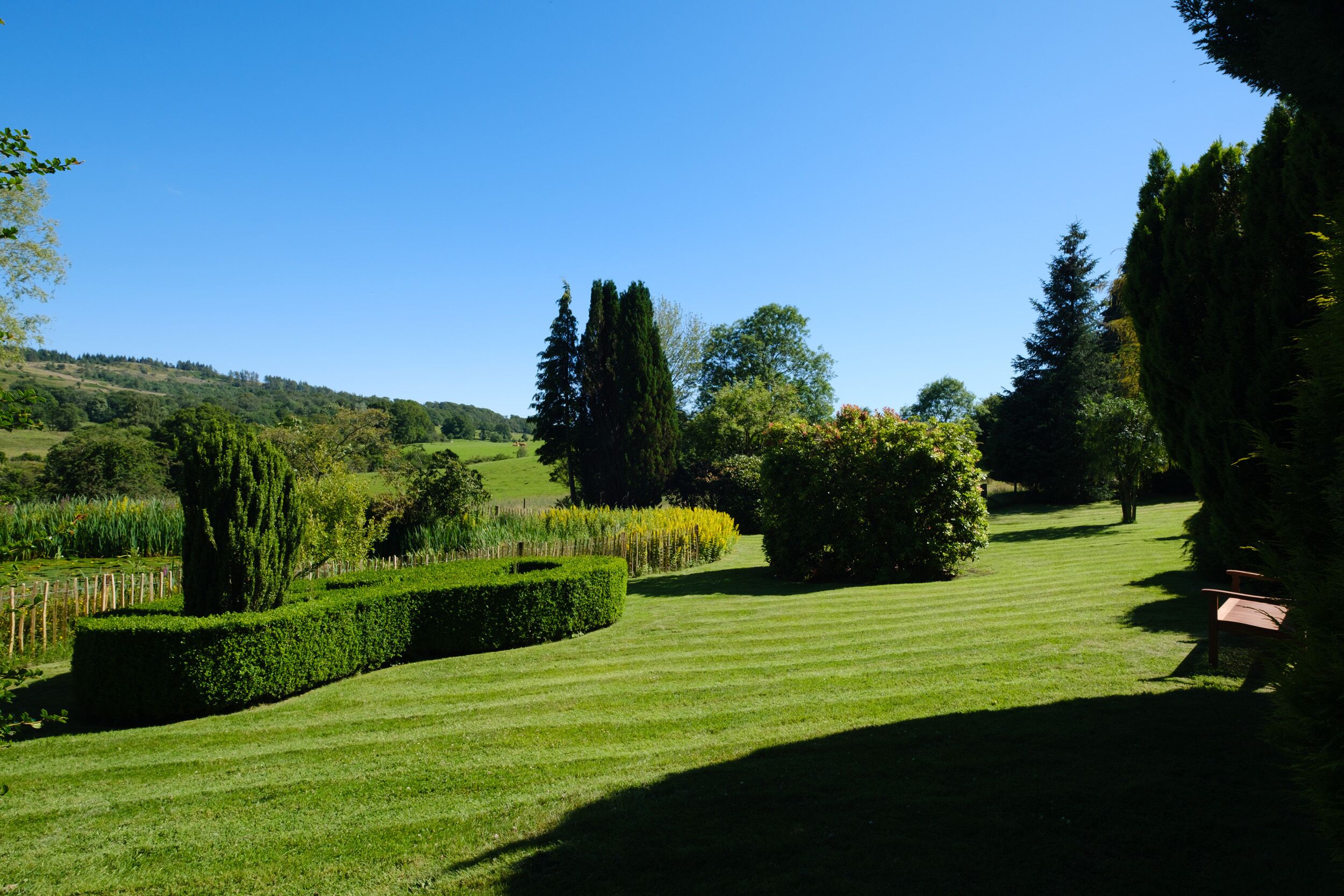 Une pelouse bien entretenue avec un banc, des haies taillées avec soin et une variété d’arbres.