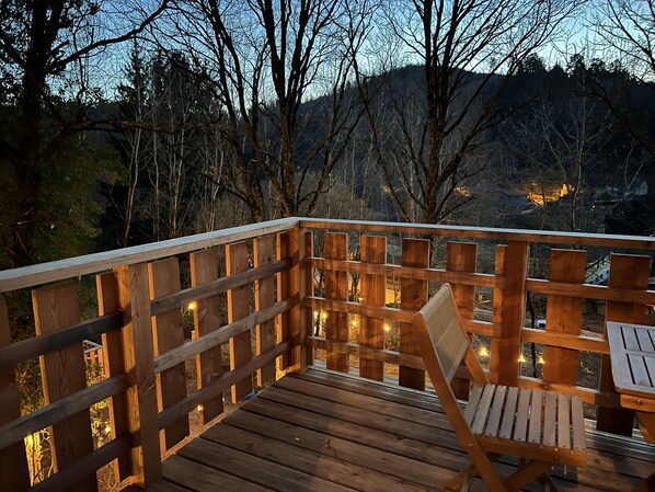Une terrasse en bois avec une chaise et une table en bois, le tout entouré d’une balustrade en bois agrémentée de lumières.