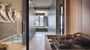 A modern spa area with a stone wall, a wooden sauna, and a glass-enclosed pool. - Wifi, fitness, swimming pool, sauna, hammam, balcony, tv, ski locker, 60m², Le Grand Bornand (Le Grand-Bornand)