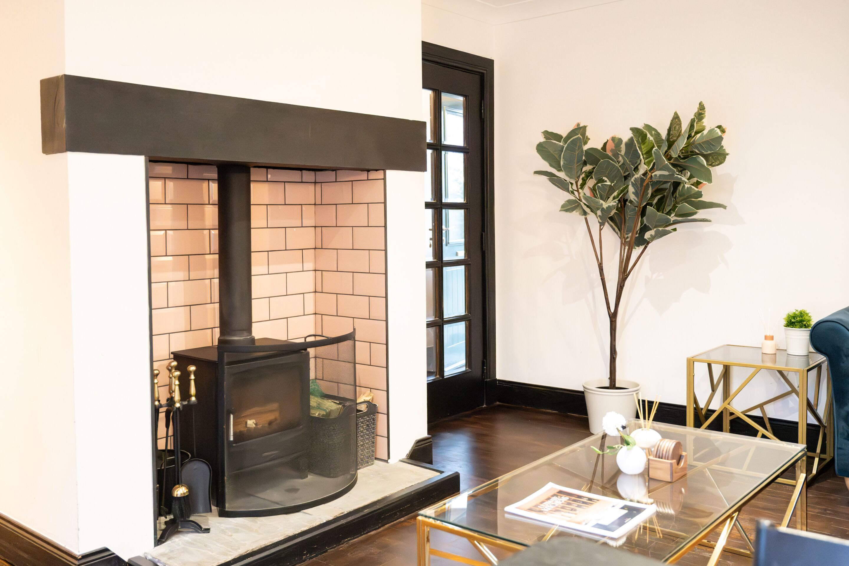 A modern living room with a fireplace, a glass coffee table, a potted plant, and a blue sofa.