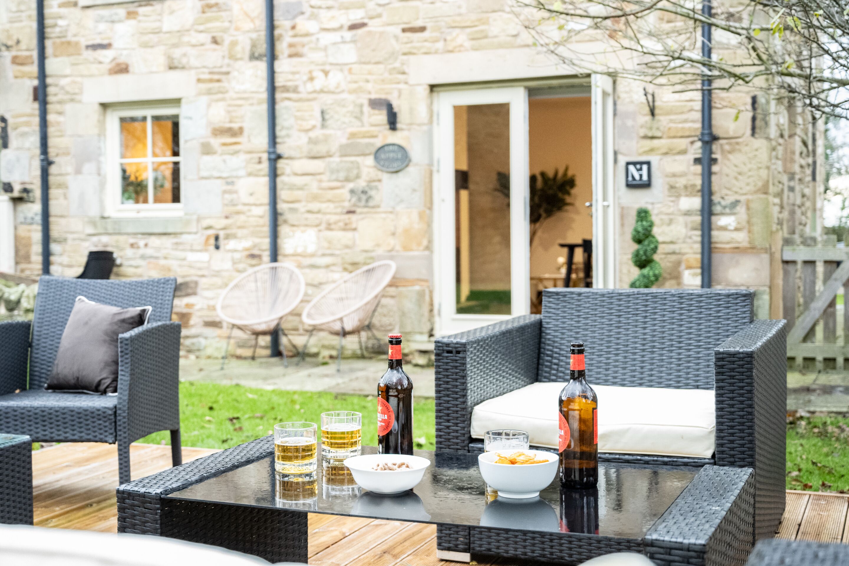 An outdoor seating area with wicker furniture, a glass table, and a stone building in the background.