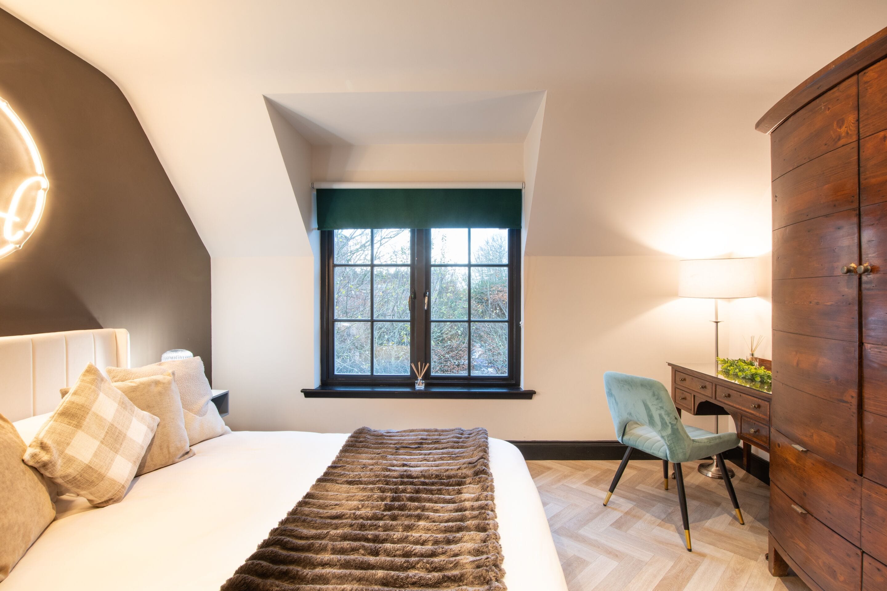 Un dormitorio con cama, escritorio, silla, armario y ventana con vistas a árboles.
