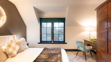 Un dormitorio con cama, escritorio, silla, armario y ventana con vistas a árboles.