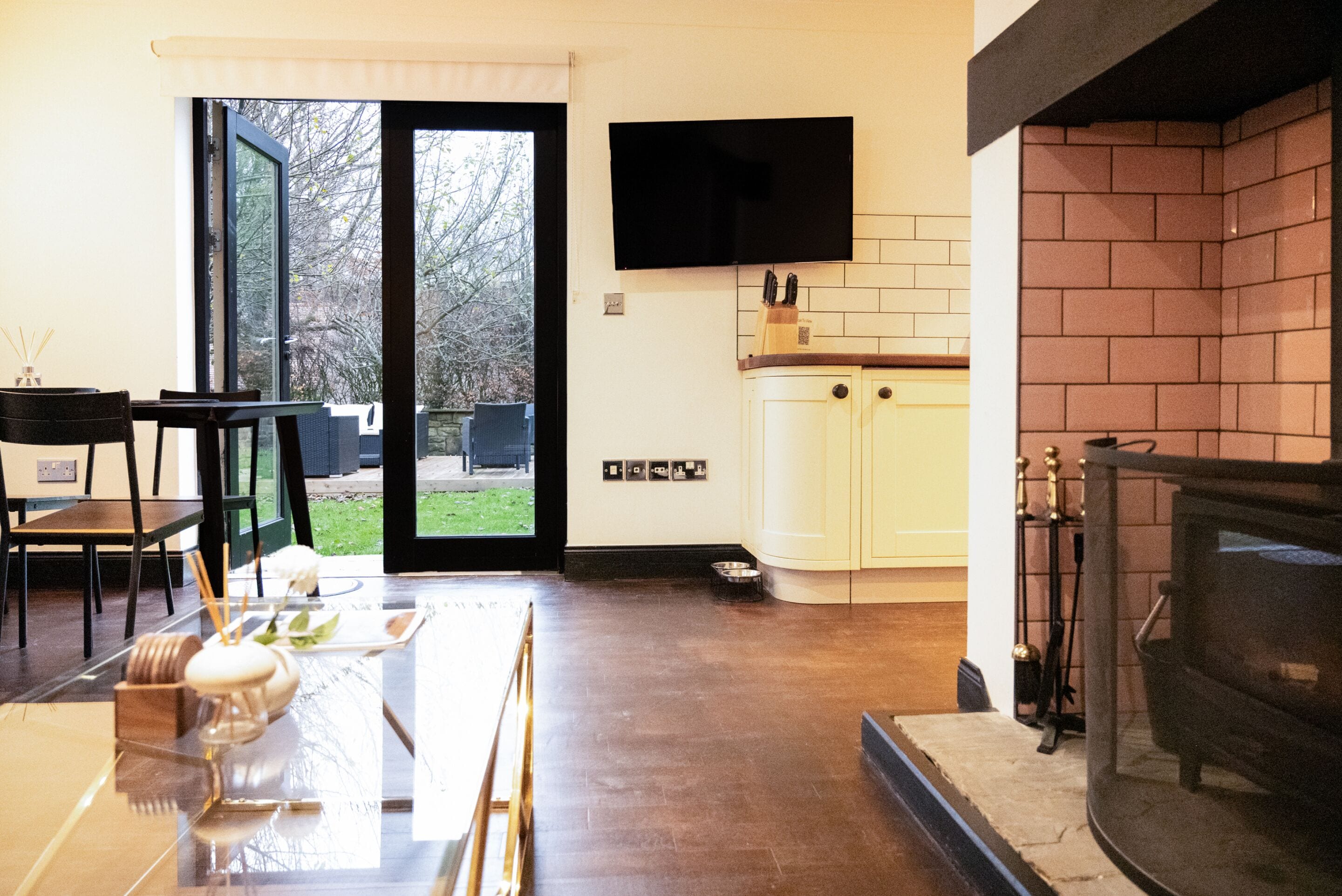 A modern kitchen with a TV mounted above the counter, a fireplace, and a sliding glass door leading to an outdoor area.