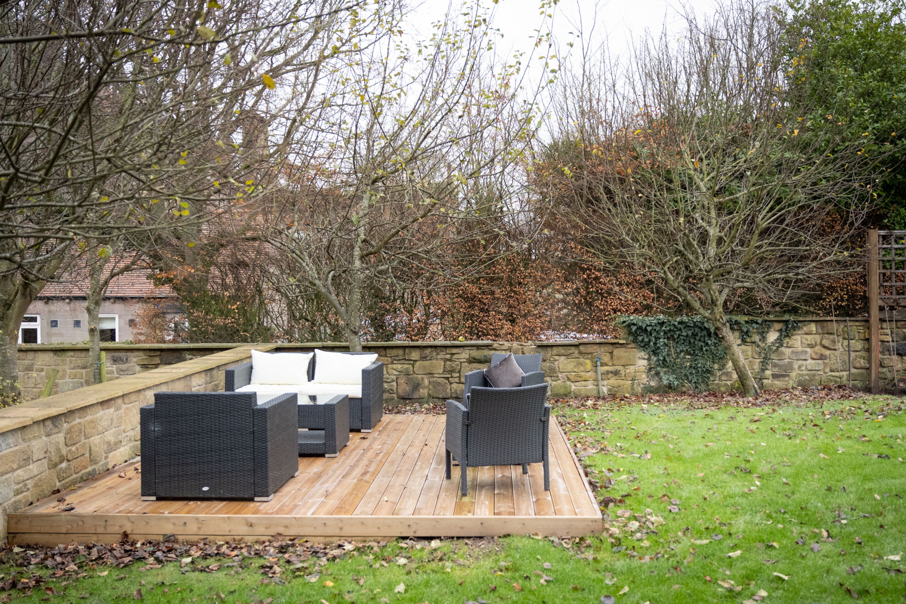 A deck with outdoor furniture, a stone wall, and a grassy area with trees.
