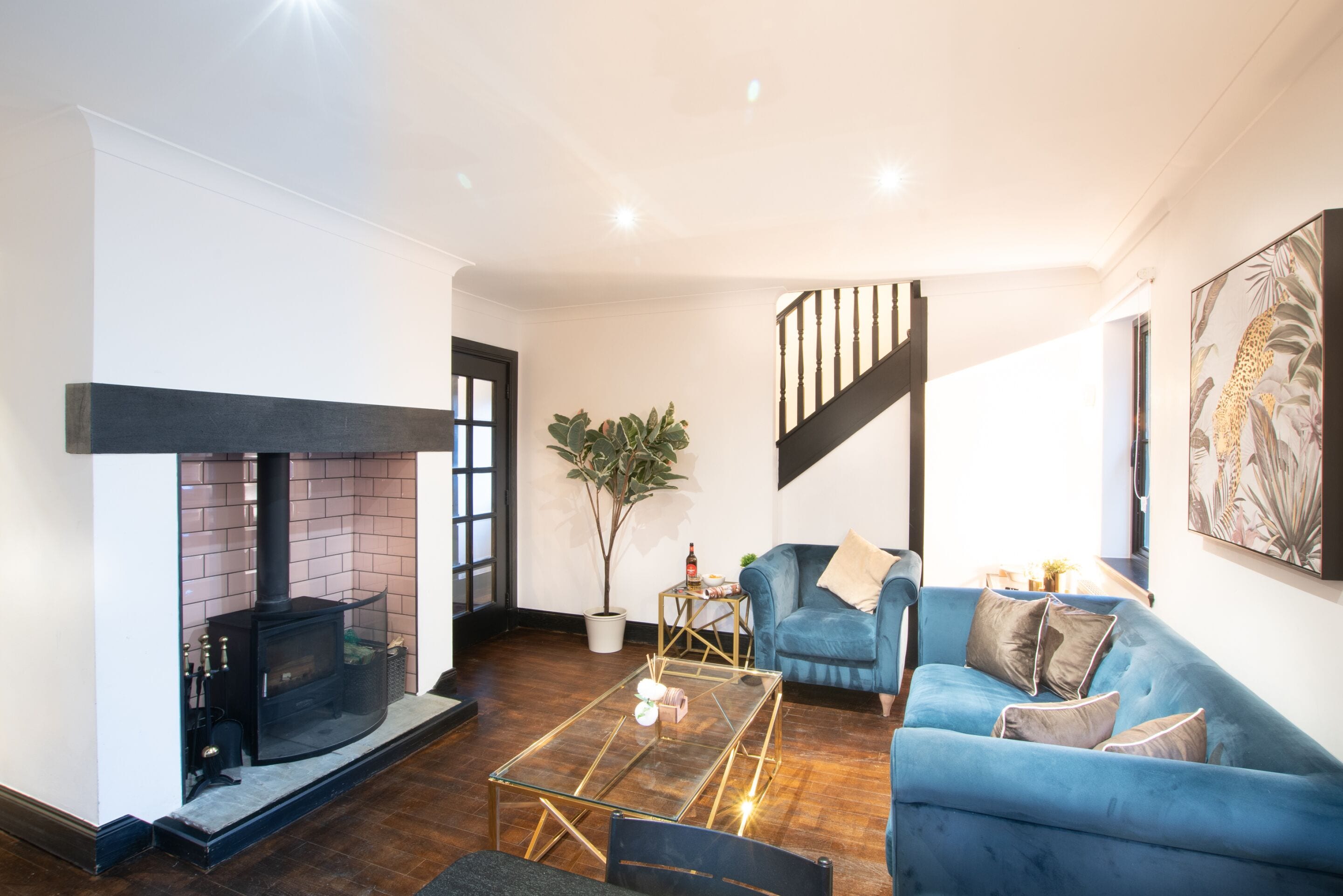 A living room with a fireplace, a blue sofa, a glass coffee table, and a staircase.