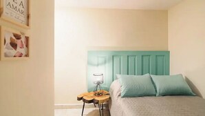 A bedroom with a teal headboard, a round wooden side table, and two light blue pillows on a bed. - Cozy corner in El Poblado! (Medellín)