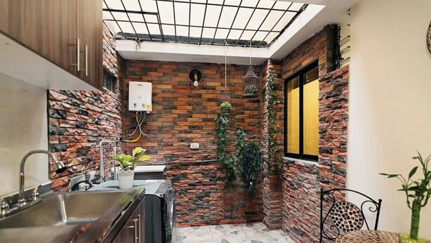 A compact kitchen with a modern design, featuring a built-in stove, a sink, and a small dining area with a table and chairs. - Cozy corner in El Poblado! (Medellín)