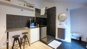 Une cuisine moderne équipée d’un four à micro-ondes encastré, d’une machine à café et d’un petit réfrigérateur. On y trouve également deux tabourets et une cabine de douche en verre.