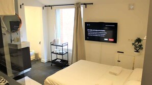 Une chambre d’hôtel avec un lit, un téléviseur fixé au mur, une petite étagère avec des articles de toilette et une fenêtre avec des rideaux.