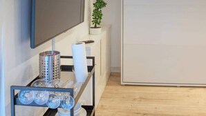 Un salon moderne avec un téléviseur à écran plat fixé au mur, une petite plante en pot, une étagère en métal avec de la vaisselle et une porte coulissante.
