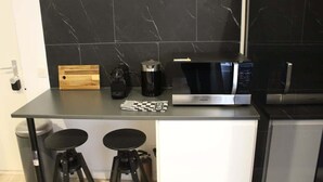 Une cuisine moderne avec un plan de travail noir, un four à micro-ondes, une machine à café et deux tabourets.