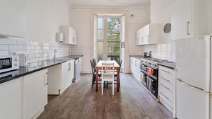 Een keuken met witte kastjes, een houten eettafel en een uitzicht door een deuropening.