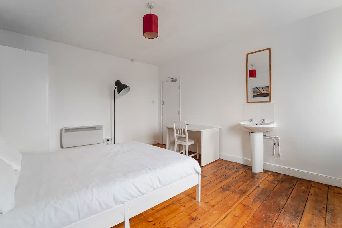 Een slaapkamer met een bed, bureau, stoel en een witte wastafel.