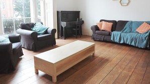 Een woonkamer met een piano, twee banken, een salontafel en een groot raam.
