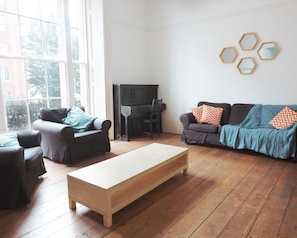 A living room with a piano, two sofas, a coffee table, and a large window. - No 64 Georgian House - By Clifton Short Lets (Bristol)