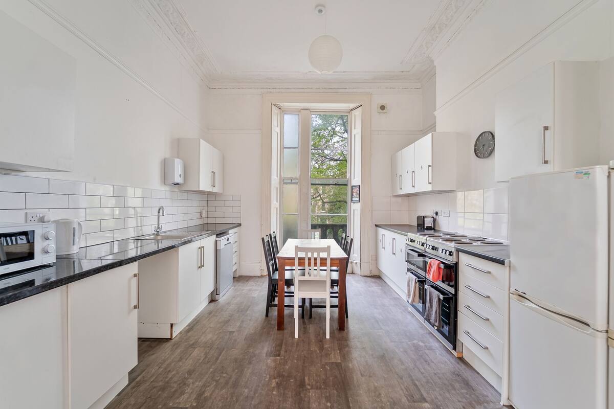 Een keuken met witte kastjes, een houten eettafel en een uitzicht door een open deur.
