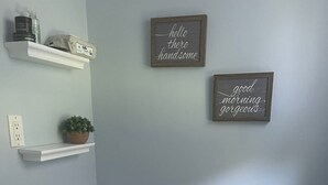 Ein Badezimmer mit Toilette, Waschbecken und Spiegel. Zwei Regale mit Pflegeprodukten und einer Topfpflanze.