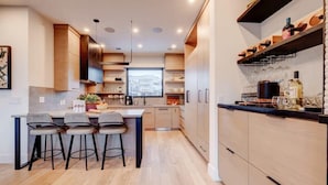 A modern kitchen with a central island, bar stools, and built-in shelves. - The Ridgeline | Ski-In 4BR Mountain Contemporary (Park City)