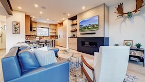 A modern living room with a blue sofa, a fireplace, and a mounted TV. - The Ridgeline | Ski-In 4BR Mountain Contemporary (Park City)