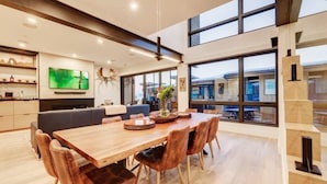 A modern dining area with a wooden table and leather chairs, a flat-screen TV mounted on the wall, and large windows offering a view of the city. - The Ridgeline | Ski-In 4BR Mountain Contemporary (Park City)