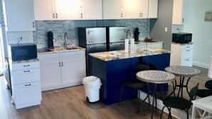 A modern kitchen with white cabinets, a blue island, and a small dining area with two round tables and chairs. - Waters Edge  - Ocean View at Symphony Beach Club! (Ormond Beach)